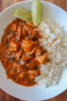 a white plate topped with rice and meat next to a slice of green leafy lime