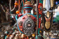 an assortment of necklaces hanging from a tree in a market place with other items on display