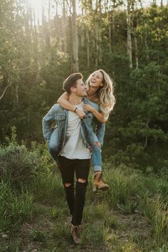 a man carrying a woman in his arms while walking through the woods with trees behind him