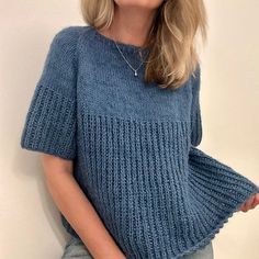 a woman wearing a blue knitted sweater posing for the camera with her hands in her pockets