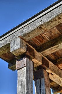 an old wooden structure with wood beams and metal brackets on the top, against a blue sky