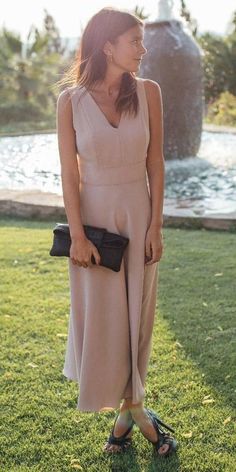 a woman standing on top of a lush green field next to a fountain wearing sandals