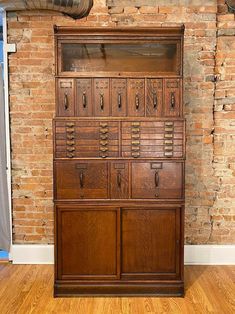 an old wooden cabinet with many drawers on it's sides in front of a brick wall