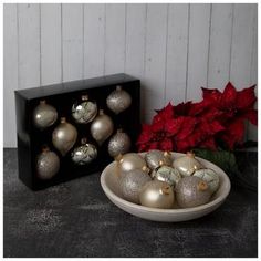 a bowl filled with silver and white ornaments next to a box of red poinsettias