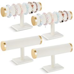 three white and gold jewelry stands with bracelets on each one stand, the other is holding several different colored beads