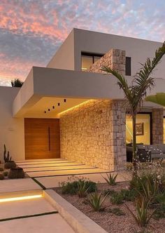 a modern house is lit up at night with palm trees in the front yard and landscaping