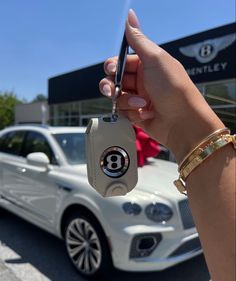 a hand holding a car key in front of a white bentley