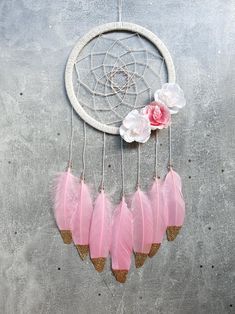 pink feathers and white flowers are hanging from a dream catcher