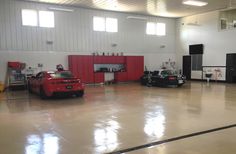 two cars parked in a large garage with red cabinets and black appliances on the walls