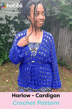 a woman with dreadlocks standing in front of a house wearing a blue crochet cardigan