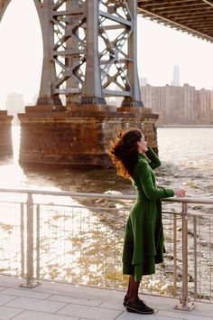 Candid photo at Domino Park in front of the Brooklyn Bridge, branding photo of woman in green coat looking out into New York City horizon over river with wind blowing through hair while leaning against rail and Brooklyn Bridge in the background Nyc Bridge, Designer Photoshoot, Bridge Photoshoot, Domino Park, Bridge Sunset, Website Photography, Williamsburg Bridge, Brooklyn Style, Headshots Women