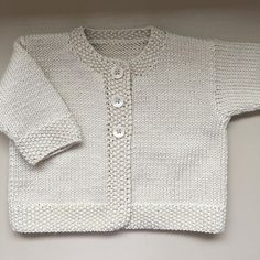 a white knitted cardigan with buttons on the front and sleeves, sitting on a shelf