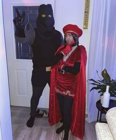 two people in costumes standing next to each other near a door with one person dressed as a black cat and the other wearing a red costume