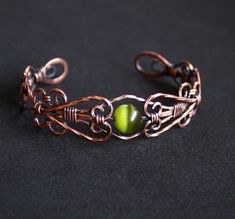 a close up of a metal bracelet on a black surface with a green bead