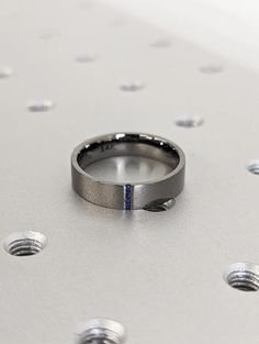 a wedding ring with a blue diamond in the center on a silver surface surrounded by screw holes