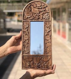 a person holding up a wooden mirror in front of a brick sidewalk with a building in the background