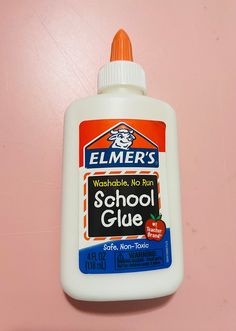 a bottle of school glue sitting on top of a pink surface