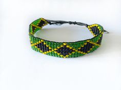 Crafted with care and attention to detail, the bracelet features a striking combination of black, green, and yellow beads arranged in the iconic Jamaican flag pattern. It is long-lasting, adjustable and designed for comfortable wear all day long.  Available in various sizes.  Wear this eye-catching bracelet with casual outfits, on special occasions, or as a statement piece to show your support for Jamaican culture, sports teams, or national events. It's perfect for fans of reggae music, Caribbea Jamaica Jewelry, Jamaica Bracelet, Jamaican Beaded Bracelet, Reggae Bracelet, Angolan Flag African Bracelets, Flag Bracelet, Jamaica Flag, Jamaican Flag, Flag Pattern