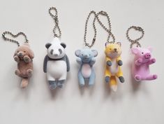 four small stuffed animals hanging from chains on a white surface with one holding a teddy bear