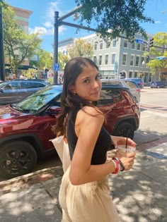 a woman walking down the street holding a drink in her hand and looking at the camera