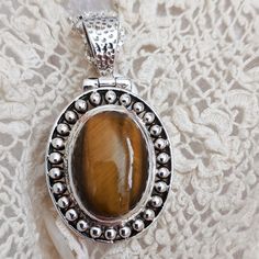 This graceful one-of-a-kind sterling silver pendant is a statement piece showcasing an oval-cut cabochon of gem-grade Tiger Eye.  A stone of vitality, strength, practicality, fairness, discernment and courage, Tiger Eye energy aids in maintaining balance between extremes: extreme's of one's own light and dark side, extreme's of one's humanity and spirit, and the extreme emotional states of joy and sorrow.  Tiger Eye allows one to make choices based upon discernment, not judgment.  It grounds the Spiritual Silver Oval Pendant Gemstone, Spiritual Silver Gemstone With Oval Pendant, Silver Necklace With Large Oval Cabochon Stone, Silver Oval Gemstone Cabochons, Silver Oval Pendant Jewelry With Large Stone, Oval Silver Natural Gemstones, Silver Jewelry With Large Oval Cabochon Pendant, Spiritual Cabochon Oval Pendant Jewelry, Spiritual Oval Cabochon Pendant Jewelry