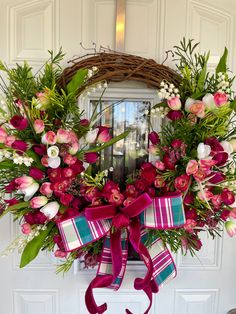 a wreath with pink and white flowers hanging on the front door, decorated with ribbon