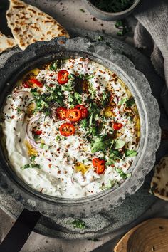 a bowl filled with hummus, tomatoes and other toppings next to pita bread