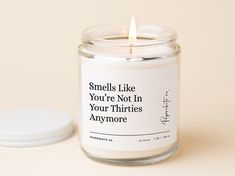 a candle that is sitting next to a white container with the words smells like you're not in your thirtiess anymore