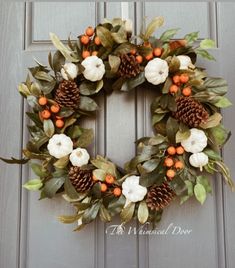 a wreath with white and orange flowers, leaves and pine cones is hanging on the front door