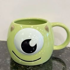 a green coffee mug with an evil eyeball on it's side sitting on a table