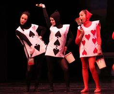 four girls dressed in costumes with hearts and spades on their chests, one holding a cup