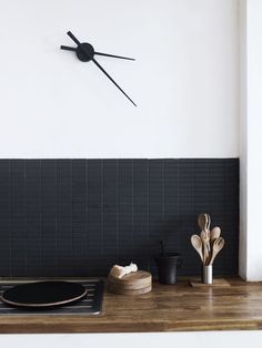 a black clock mounted on the side of a white wall next to a stove top