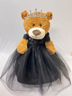 a brown teddy bear wearing a black dress with a tiara on it's head