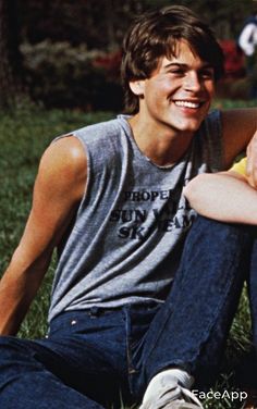 a young man sitting in the grass with his arms crossed