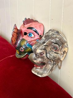 two masks sitting on top of a red velvet chair next to a white painted wall