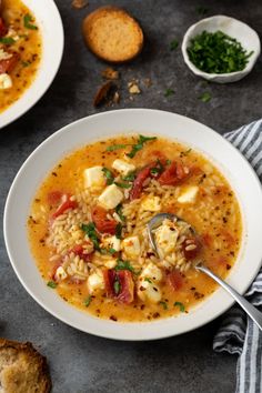 two white bowls filled with soup next to bread and spoons on a gray surface