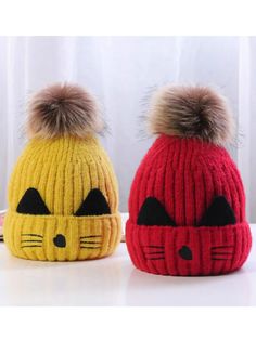 two knitted hats with cats on them, one is yellow and the other is red