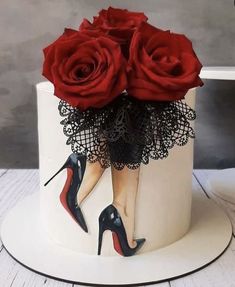 a white cake with red roses and high heels on it's side, decorated with black lace