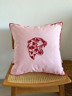 a pink pillow with a red and white tiger on it sitting on a wooden chair