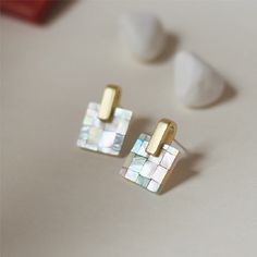 two square shaped earrings with gold posts on top of a table next to marshmallows