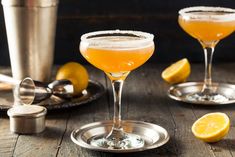 two cocktail glasses filled with orange juice and topped with sugar sit on a wooden table