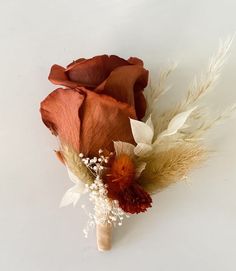 a red rose and some white flowers on a white table top with dried grass in the foreground