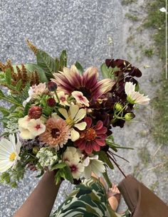 a bouquet of flowers in someone's hand on the ground with grass and rocks