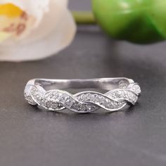 a white gold wedding band with diamonds on the bottom and side, sitting next to a flower