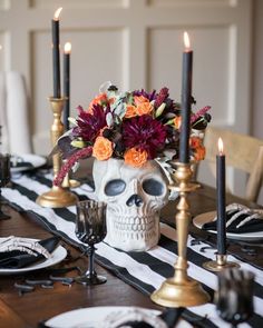 a table with black and white striped cloth, gold candlesticks and a skull head decorated with flowers