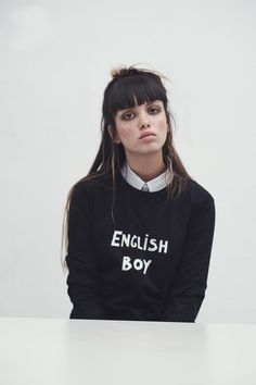 a young woman sitting at a table with her hands on her hips wearing a sweater that says english boy