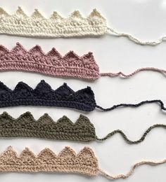 five crocheted headbands are lined up on a white surface, each with different colors