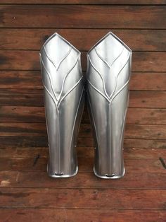 two silver metal vases sitting on top of a wooden floor next to each other