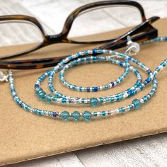 Dainty and bohemian eyeglass necklace chain made with tiny Preciosa Czech crystal seed beads in blue tones and small round faceted cubic zirconia crystals.   Paired with beautiful blue cz gems, this handmade eyeglass chain will definitely create a unique look. This eyeglass lanyard is made on strong quality beading wire with silver plated wire guardians that protect the eyeglass holder grips. The necklace is ended with spring clasps that hold the eyeglass grips and they can be easily removed to Adjustable Glass Beaded Necklaces With Tiny Beads, Adjustable Glass Beaded Necklace With Tiny Beads, Adjustable Tiny Beaded Glass Necklaces, Adjustable Tiny Beaded Glass Necklace, Adjustable Glass Necklaces With Tiny Beads, Adjustable Glass Necklace With Tiny Beads, Adjustable Silver Glasses Chains With Colorful Beads, Handmade Adjustable Blue Glasses Chains, Handmade Adjustable Turquoise Glasses Chains