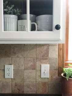 a kitchen with white cabinets and tile backsplash, coffee mugs on the window sill